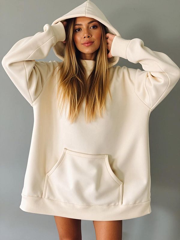 A young woman poses in a light beige oversized hoodie against a neutral background.