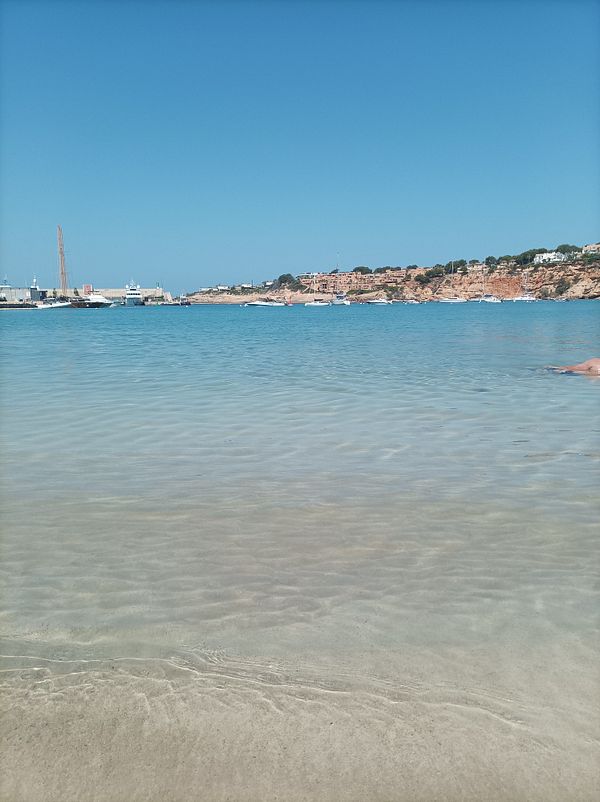 A serene view of a calm beach with clear water and a distant shoreline.