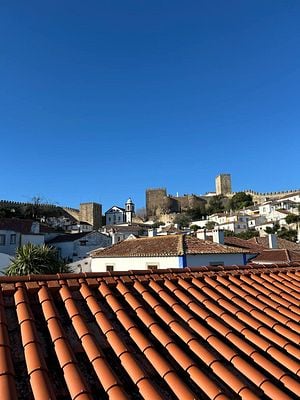 A picturesque view of a medieval town in Portugal featuring terracotta rooftops and a castle.