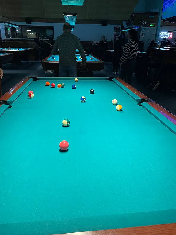 A group of friends is playing pool in a dimly lit billiards hall in Amsterdam.