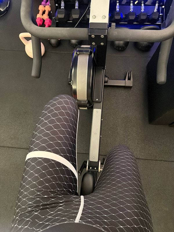 Photo of athletic man sitting on gym floor resting post-exercise, with workout gear and sports shoes visible.