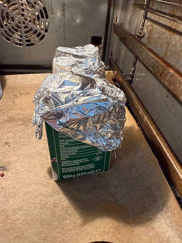 Two wrapped containers are placed inside an oven on a baking sheet.