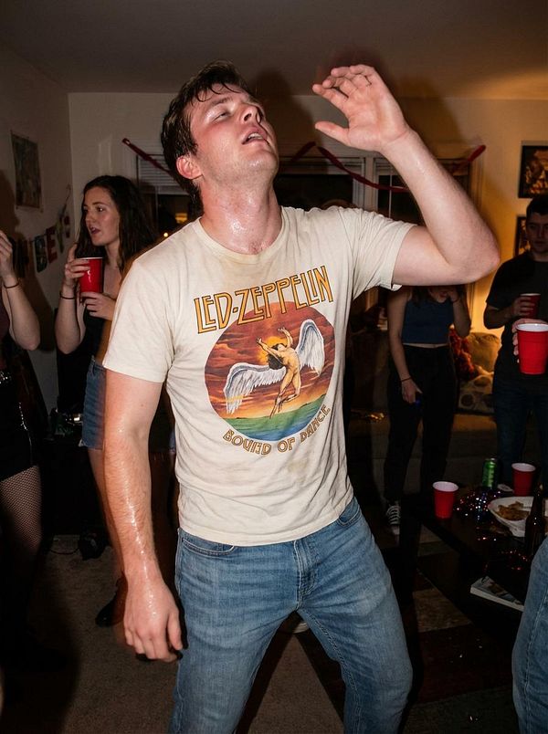 A young man dances energetically at a lively party, surrounded by friends.