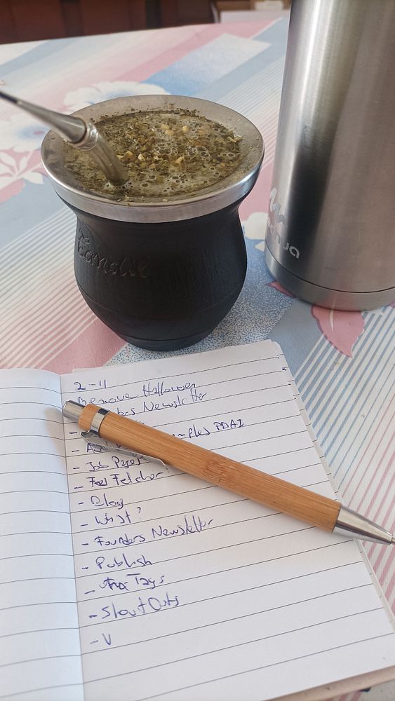 A cozy workspace featuring a traditional mate drink, a notebook with tasks, and a pen.