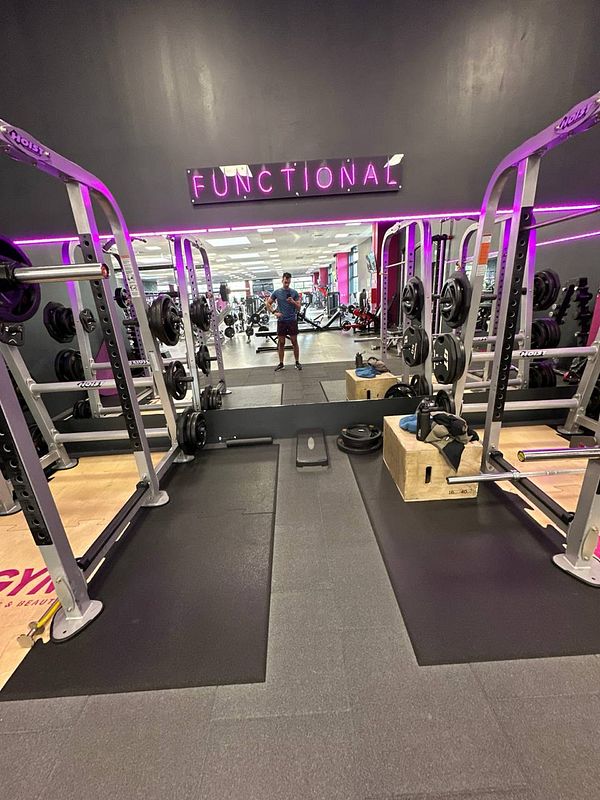 A gym interior featuring weightlifting equipment and a person preparing for a workout.
