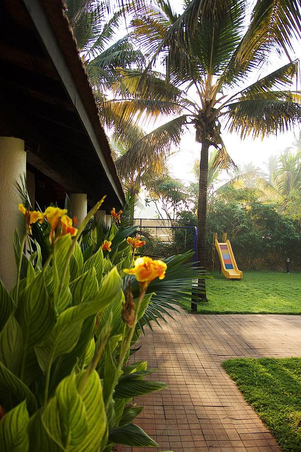 A serene garden scene featuring tropical plants, a playground slide, and palm trees.