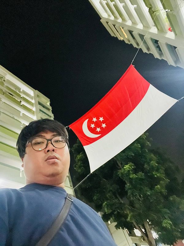 A person stands under a Singaporean flag at night.