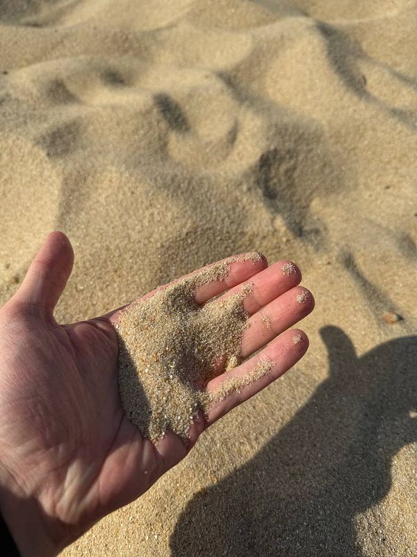 A hand is holding sand against a backdrop of a sandy beach.