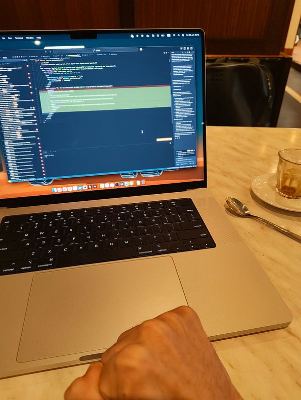 A laptop displaying code is positioned on a table next to an espresso and a spoon.