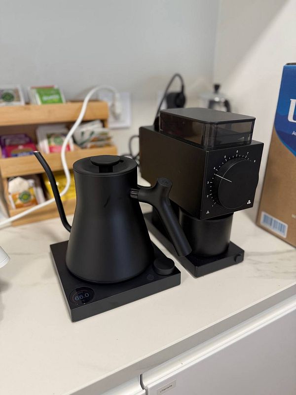A black Fellow EKG Pro kettle is positioned next to a black grinder on a countertop.