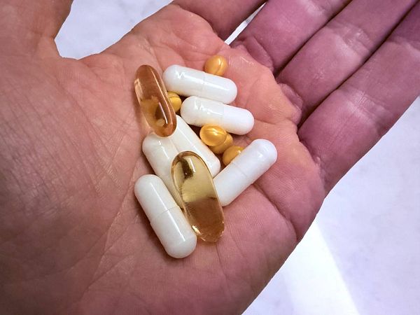 A hand holds a variety of dietary supplements, showcasing a mix of capsules and soft gels.