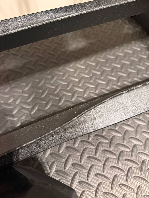 Close-up of a gym equipment rack with visible twisted steel causing a defect.