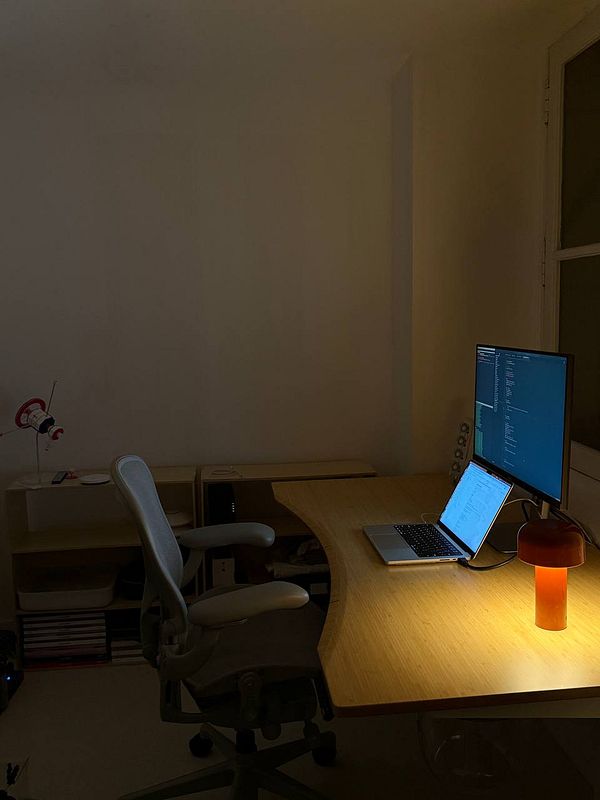 A dimly lit office space featuring a desk with a laptop and a monitor.