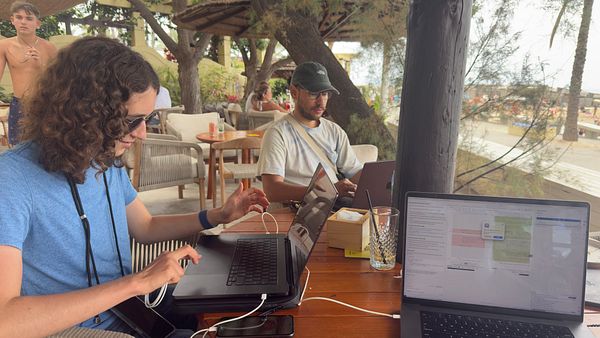 A group of individuals is working on laptops at a beachside café.