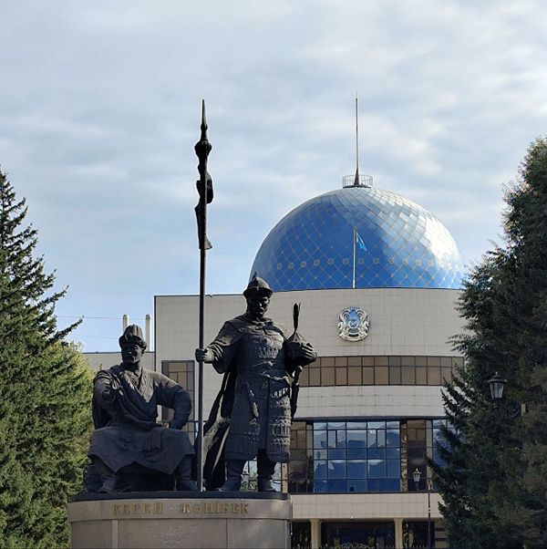 Statue of Kerei and Zhanibek in front of a building with a blue dome in Astana, Kazakhstan.