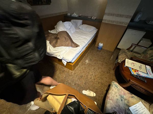 A small, somewhat cluttered room with a bed and seating area.