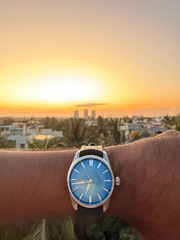 A wristwatch is prominently displayed against a vibrant sunset backdrop.