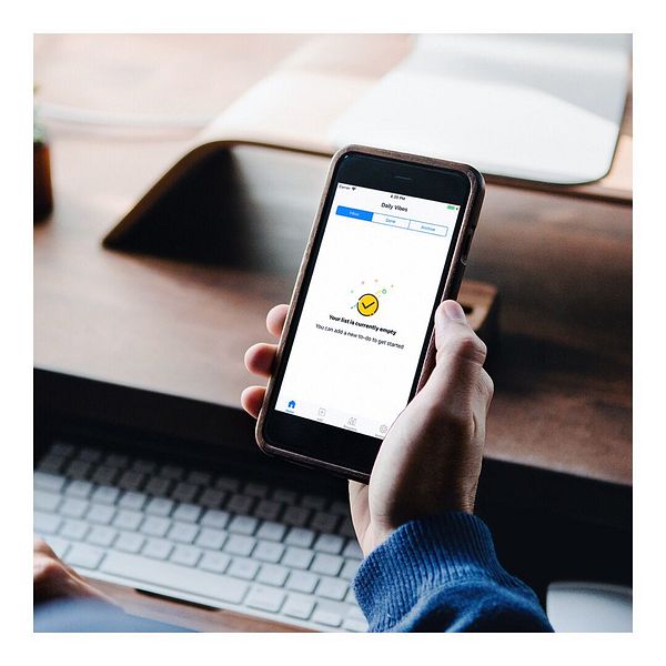 A person is holding a smartphone displaying a task management app with an empty task list.