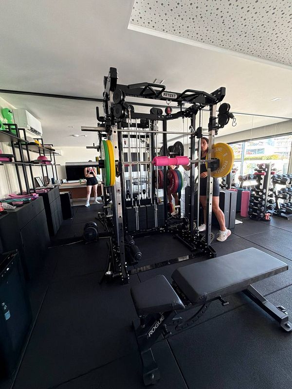 Photograph of a gym interior with various workout equipment including weights, benches, and squat racks.