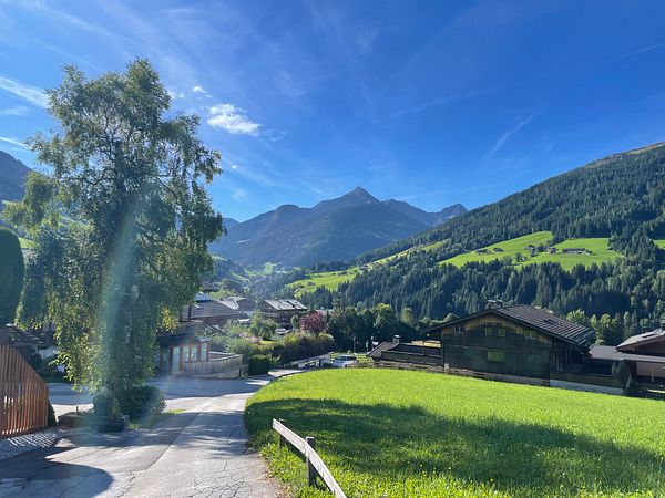 A picturesque landscape featuring mountains, lush greenery, and traditional wooden houses under a clear blue sky.