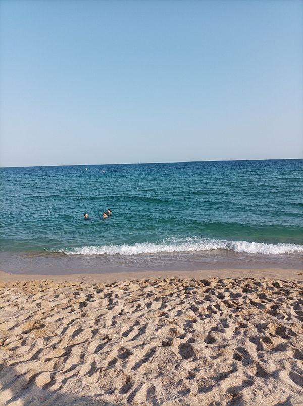 A serene beach scene in Barcelona with swimmers in the water.