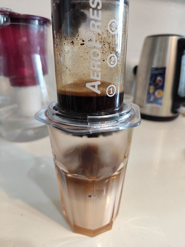 An Aeropress coffee maker is in use, extracting coffee into a glass below.