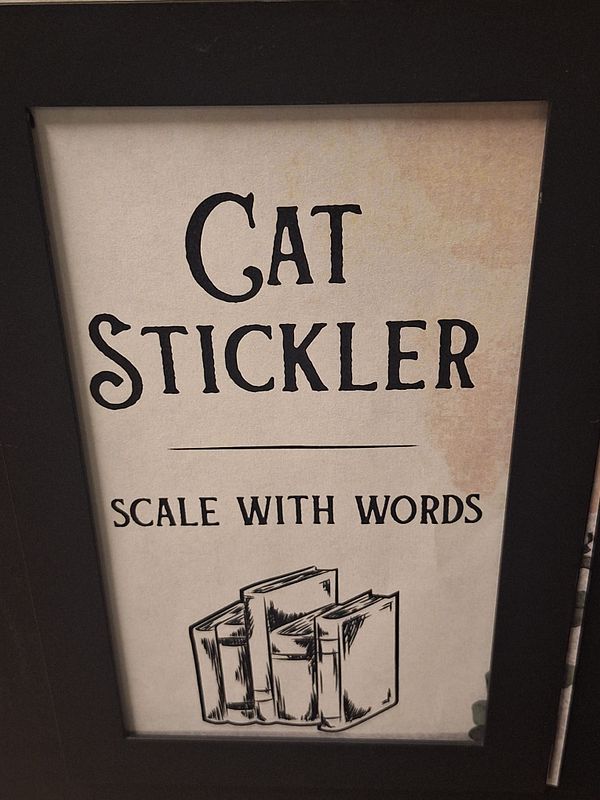 A personalized desk marker featuring the name 'Cat Stickler' and a tagline 'SCALE WITH WORDS'.