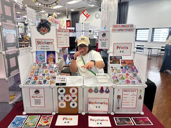 A vendor is showcasing handmade art products at a convention booth.