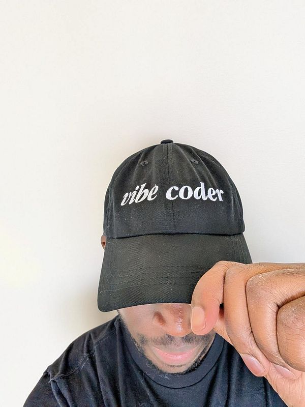 A person is wearing a black cap with the phrase 'vibe coder' embroidered on it.