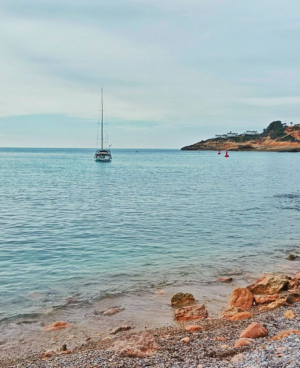A serene coastal scene featuring a sailboat on calm waters near a rocky shore.