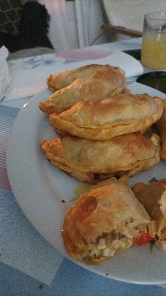 Close-up of several golden homemade empanadas arranged on a serving plate with parsley garnish.