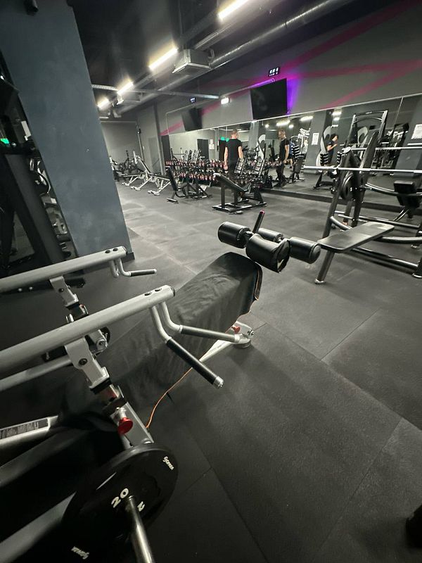 A gym interior featuring various workout equipment and individuals exercising.