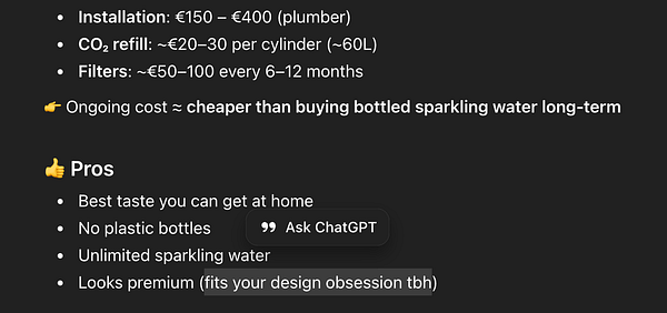 A white and blue robot model holding a reflective helmet stands outdoors on a paved surface with a background of orange, fluffy clouds and a blue sky.