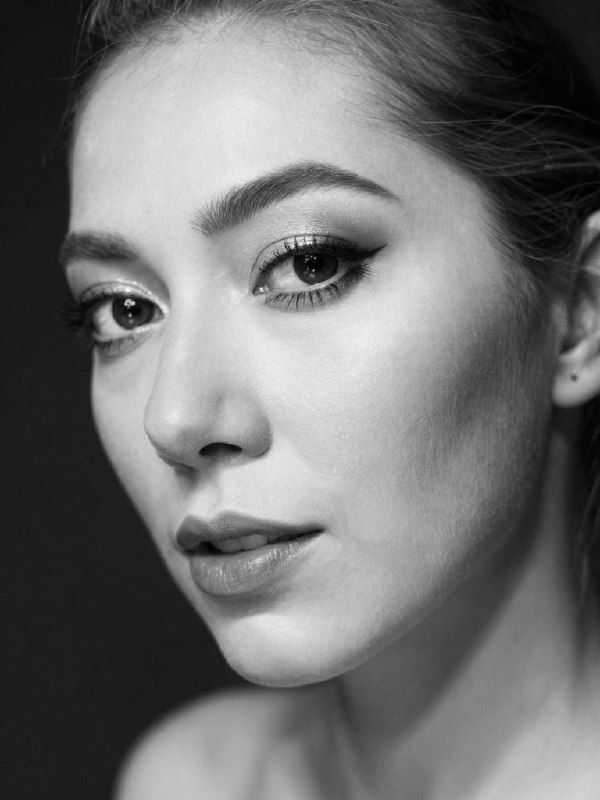 A young man with curly hair wearing glasses and headphones is seated at a desk using a laptop with text on the screen.