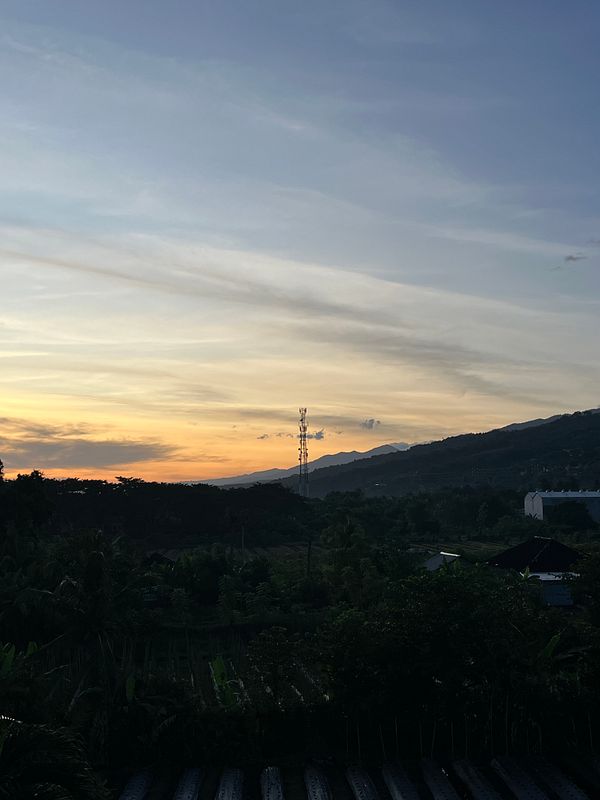 A serene landscape at dawn featuring a colorful sky and a distant cell tower.