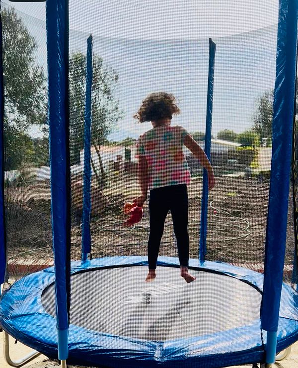 A young girl is joyfully jumping on a newly assembled trampoline while holding a toy.
