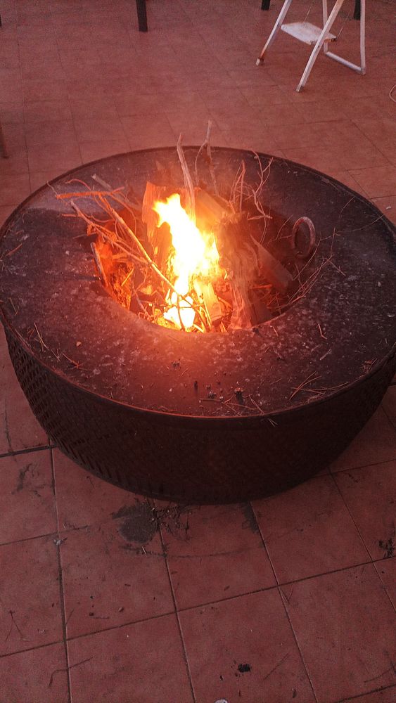 A fire burns brightly in a circular fire pit surrounded by a tiled floor.