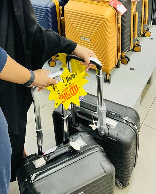 A person is holding two small black luggage pieces in a store.