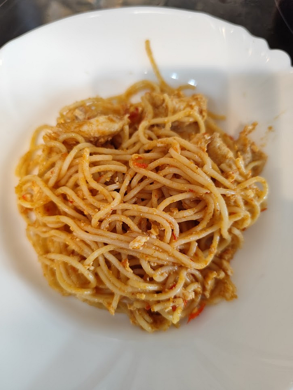A plate of tom-yum pasta is presented in a white dish.