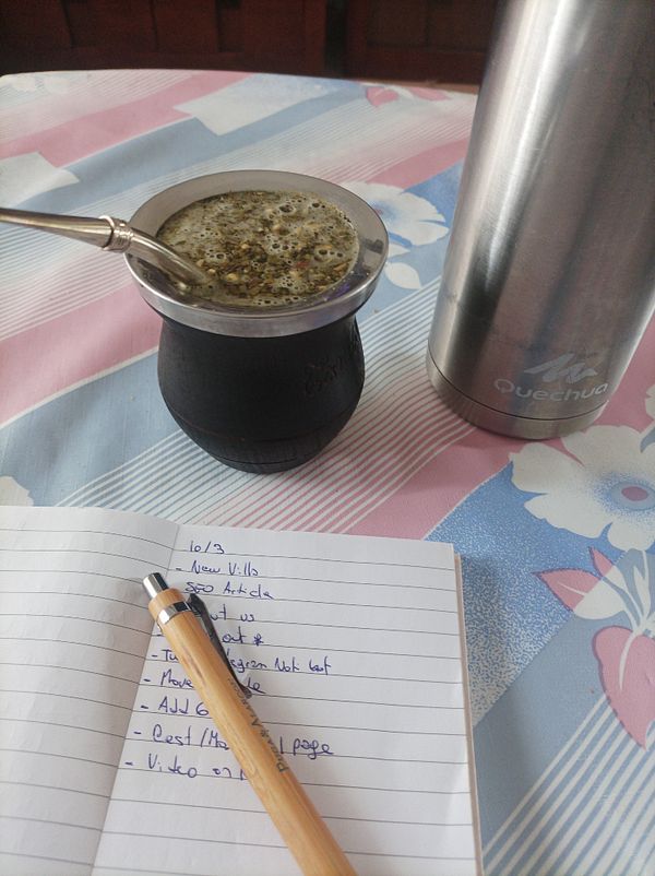A cozy workspace featuring a traditional mate drink, a thermos, and a notebook with a to-do list.