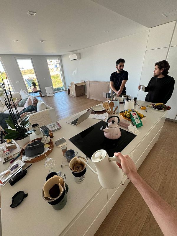 A cozy coworking space with two people preparing coffee while another relaxes on a couch.