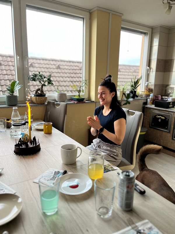 A woman celebrates her birthday with a cake and drinks in a cozy kitchen setting.