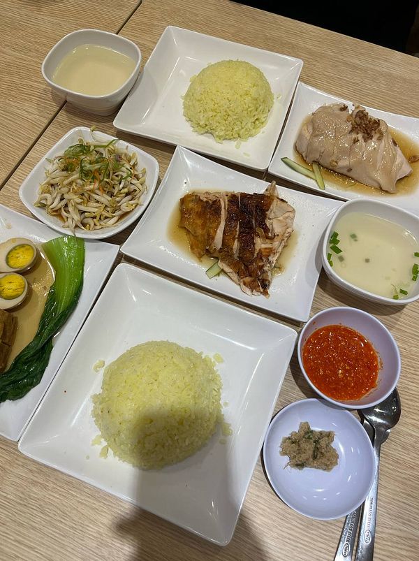 A delicious spread of chicken rice and accompanying dishes is presented on a wooden table.