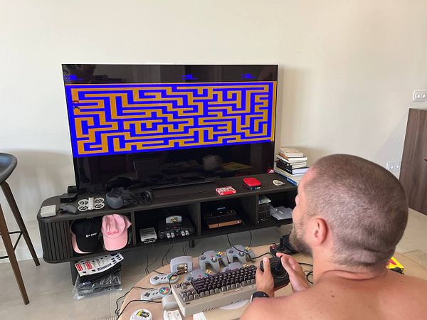 A person is playing a retro-style maze game on a large TV while seated in a casual living room setup.
