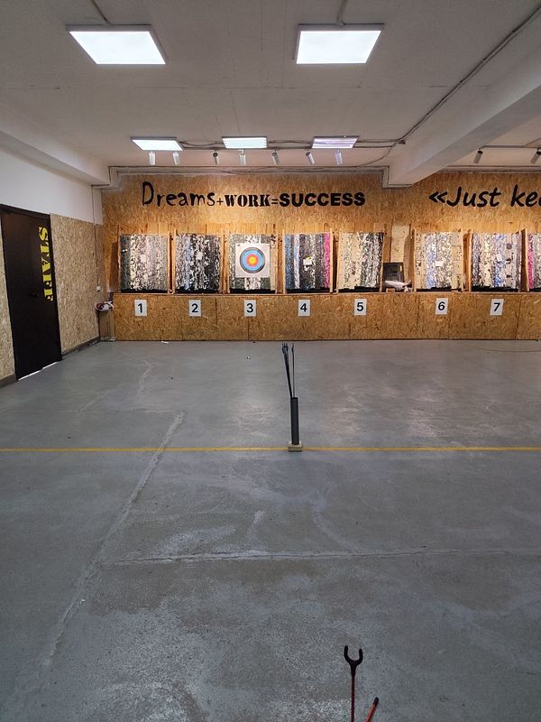 Indoor archery range with seven numbered target boards and motivational text on the wall.