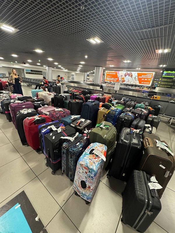 A chaotic scene at Lisbon Airport with numerous pieces of luggage scattered around.