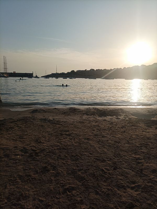 A serene beach scene at sunset with swimmers in the water.