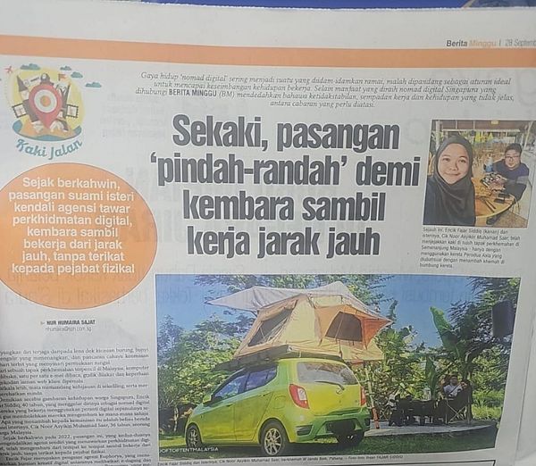 The image features a newspaper article from Berita Harian discussing a couple's digital nomad lifestyle.