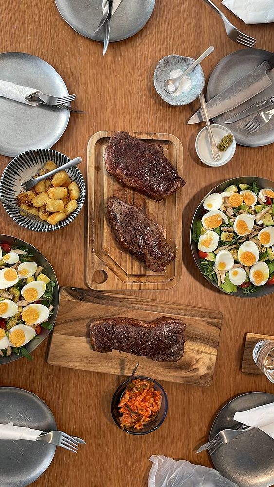 A grilled steak served on a white plate accompanied by a small cup of sauce and a side of vegetables.