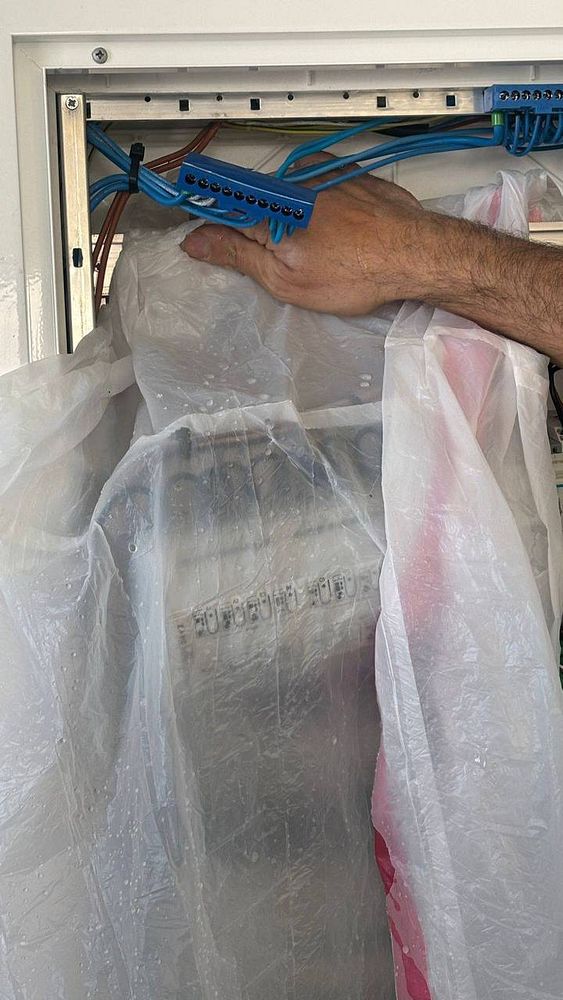 A technician is inspecting an electrical box covered with a plastic sheet, revealing water damage due to improper installation.